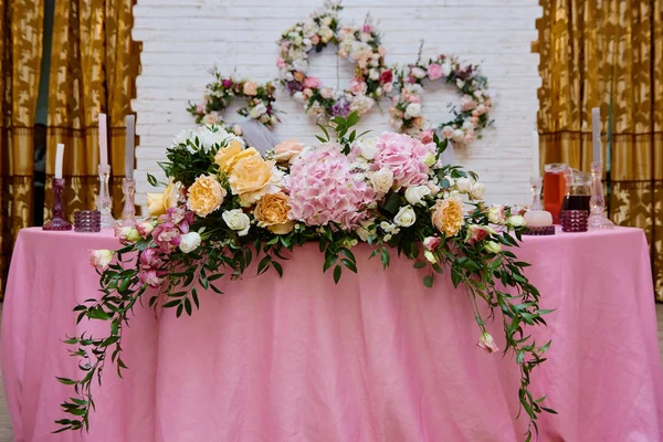 Пышные цветочные композиции на свадебном столе на открытом воздухе. Свадебный президиум в ресторане, копировальное пространство. Банкетный стол для молодоженов с розовыми и оранжевыми цветами роз. Роскошные свадебные украшения — стоковое фото