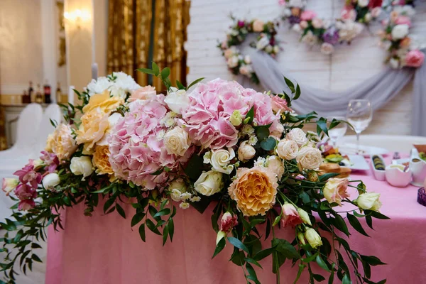 Пышные цветочные композиции на свадебном столе на открытом воздухе. Свадебный президиум в ресторане, копировальное пространство. Банкетный стол для молодоженов с розовыми и оранжевыми цветами роз. Роскошные свадебные украшения — стоковое фото