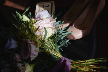 Pembe, mor güller ve yeşillik gelin buketi, bej kadın ayakkabıları, ahşap takvim ve siyah arka planda altın alyanslar, kopya alanı. Düğün konsepti