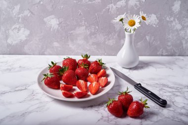 Beyaz seramik kasede kırmızı çilek ve gri arka planda papatya çiçekleri, kopyalama alanı. Sağlıklı gıda konsepti, natürmort