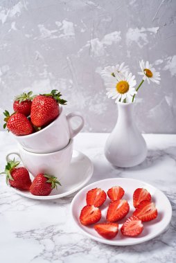 Beyaz seramik kasede olgun organik çilekler ve gri beton arka planda papatya çayı, kopyalama alanı. Sağlıklı gıda konsepti, natürmort