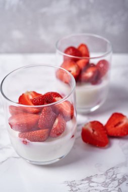 Beyaz masa arkasında taze dilimlenmiş çilekli iki bardak sağlıklı yoğurt, kopyalama alanı. Sağlıklı kahvaltı, yemek konsepti