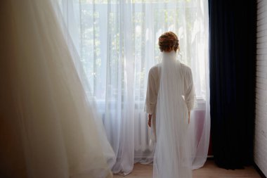 Beyaz ipek sabahlık güzel gelin portresi kıvırcık saç modeli ve peçe yatak odasında pencere yakınında duran, kopya alanı. Gelinin sabah hazırlığı. Geri görünüm