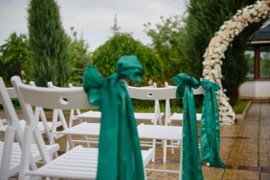 Kemer yolu çıkışlarının her iki tarafında zümrüt şeritli beyaz düğün sandalyeleri, kopyalama alanı. Boş tahta sandalyeler düğün töreni için hazırlanıyor.