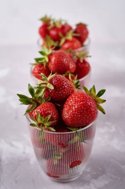 Gri masa zemininde cam kaselerde kırmızı çilekler, kopyalama alanı. Sağlıklı gıda konsepti