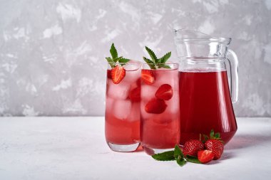Buzlu taze çilekli limonata ve bardakta nane şekeri ve beyaz masada sürahi, kopyalama alanı. Soğuk yaz içkisi. Meyve kokteyli ile köpüklü cam.
