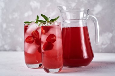 Buzlu taze çilekli limonata ve bardakta nane şekeri ve beyaz masada sürahi, kopyalama alanı. Soğuk yaz içkisi. Meyve kokteyli ile köpüklü cam.