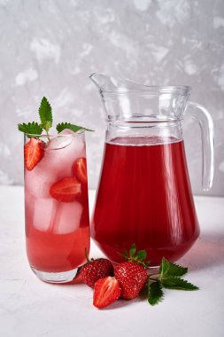 Buzlu taze çilekli limonata ve bardakta nane şekeri ve beyaz masada sürahi, kopyalama alanı. Soğuk yaz içkisi. Meyve kokteyli ile köpüklü cam.