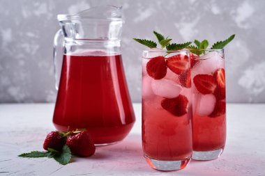 Buzlu taze çilekli limonata ve bardakta nane şekeri ve beyaz masada sürahi, kopyalama alanı. Soğuk yaz içkisi. Meyve kokteyli ile köpüklü cam.