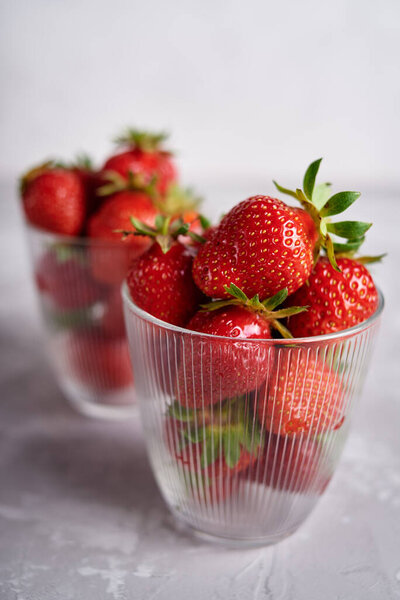 Red ripe strawberries in glass bowls on gray table background, copy space. Healthy food concept