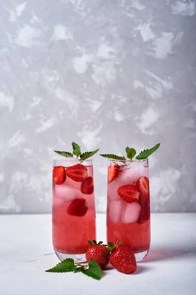 Fresh strawberry lemonade with ice and mint in glass on table, copy space. Cold summer drink. Sparkling glasses with berry cocktail
