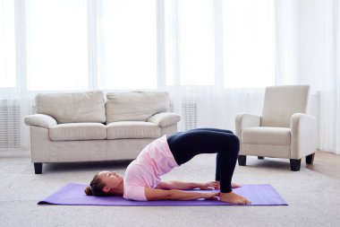 Evdeki minderin üzerinde Kandharasana (omuz pozu) uygulayan genç kadının portresi, fotokopi alanı. Yoga çalışıyorum. Sağlık ve sağlıklı yaşam tarzı