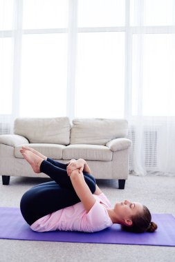 Evde, fotokopi odasında apanasana pozu veren genç bir kadının portresi. Apanasana. Dizler göğüs pozuna. Yoga çalışıyorum. Sağlık ve sağlıklı yaşam tarzı