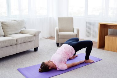 Evdeki minderin üzerinde Kandharasana (omuz pozu) uygulayan genç kadının portresi, fotokopi alanı. Yoga çalışıyorum. Sağlık ve sağlıklı yaşam tarzı