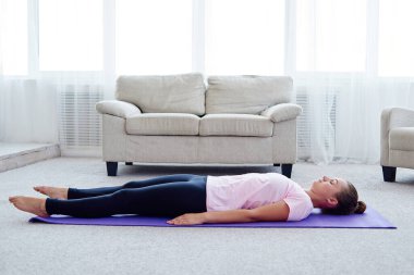 Young woman lying on yoga mat with eyes closed in savasana pose at home. Fitness, sport and healthy lifestyle concept. Corpse pose clipart