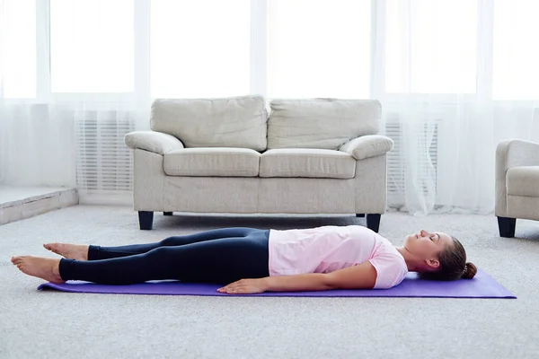 Savasana'da gözleri kapalı yoga minderinde yatan genç kadın evde poz veriyor. Fitness, spor ve sağlıklı yaşam tarzı kavramı. Ceset pozu