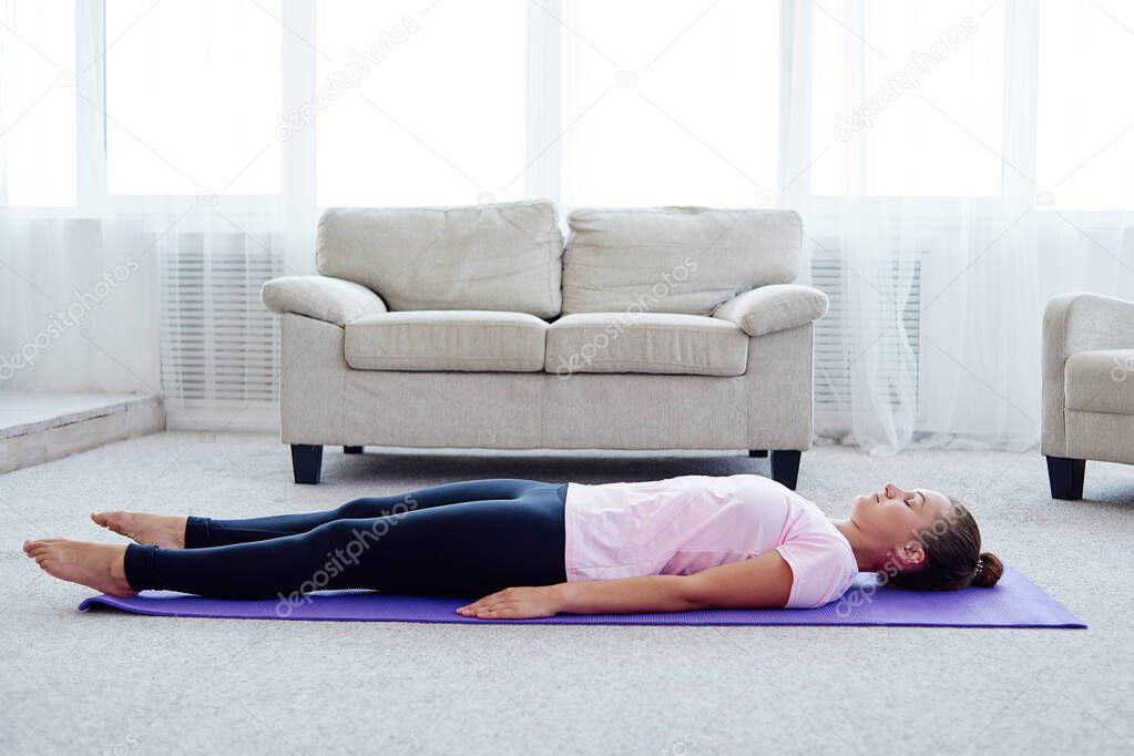 Young woman lying on yoga mat with eyes closed in savasana pose at home. Fitness, sport and healthy lifestyle concept. Corpse pose