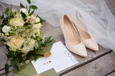 Lüks düğün davetiyeleri, alyanslar, zarif gelin ayakkabıları ve ahşap arka planda gelin buketi. Balayı ve düğün konsepti