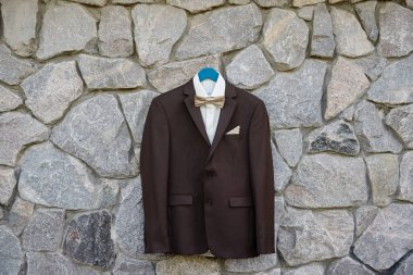 Açık havada taş duvarda asılı beyaz gömlekli ve papyonlu zarif kahverengi erkek smokin, kopyalama alanı. Modern erkek aksesuarları. Düğün detayları 