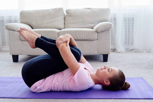 Evde, fotokopi odasında apanasana pozu veren genç bir kadının portresi. Apanasana. Dizler göğüs pozuna. Yoga çalışıyorum. Sağlık ve sağlıklı yaşam tarzı