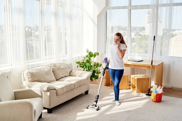 Wanita Muda Berbaju Putih Memegang Vacuum Cleaner Dan Berbicara Ponsel — Stok Foto