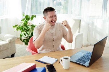 Heyecanlı genç adam yumruklarını kaldırarak zafer kazanıyor. Mutlu adam görevini tamamladı ve görevdeki başarısını kutladı. Ben bir kazananım! Ah evet! Yaptım! Yapılan işten memnun.