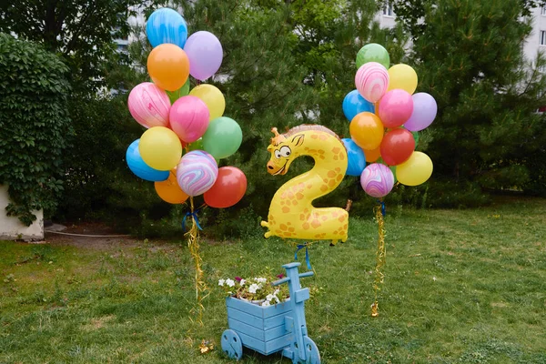 Anniversary or birthday photo zone with yellow, blue, green, red, orange and violet balloons outdoors, copy space. Colorful balloons, two years