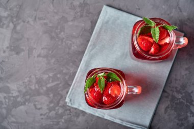 Gri beton masa arkaplanında naneli ev yapımı çilek çayı, kopyalama alanı. Köpüklü bardaklarda soğuk yaz meyvesi içeceği. Taze vitamin içeceği.