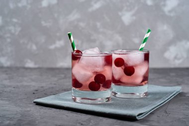 Buzlu taze vişneli limonata, nane ve kağıt kamışla gri masa zemininde köpüklü bardaklar, kopyalama alanı. Soğuk yaz içkisi. Meyve kokteyli.