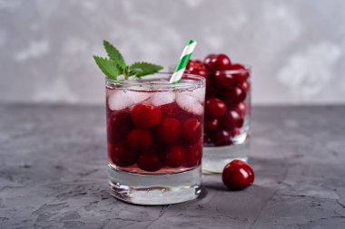 Buzlu taze vişneli limonata, nane ve kağıt kamışla gri masa zemininde köpüklü bardaklar, kopyalama alanı. Soğuk yaz içkisi. Meyve kokteyli.