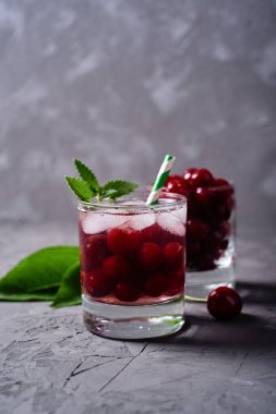 Buzlu taze vişneli limonata, nane ve kağıt kamışla gri masa zemininde köpüklü bardaklar, kopyalama alanı. Soğuk yaz içkisi. Meyve kokteyli.