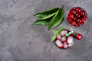 Buzlu taze vişneli limonata, nane ve kağıt kamışla gri masa zemininde köpüklü bardaklar, kopyalama alanı. Soğuk yaz içkisi. Meyve kokteyli.