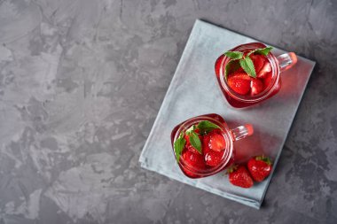 Gri beton masa arkaplanında naneli ev yapımı çilek çayı, kopyalama alanı. Köpüklü bardaklarda soğuk yaz meyvesi içeceği. Taze vitamin içeceği.