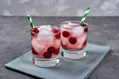 Buzlu taze vişneli limonata, nane ve kağıt kamışla gri masa zemininde köpüklü bardaklar, kopyalama alanı. Soğuk yaz içkisi. Meyve kokteyli.