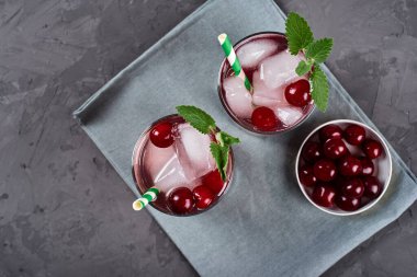 Buzlu taze vişneli limonata, nane ve kağıt kamışla gri masa zemininde köpüklü bardaklar, kopyalama alanı. Soğuk yaz içkisi. Meyve kokteyli.