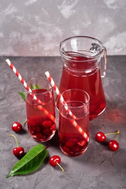 Taze vişneli limonata bardakta kağıt kamış ve gri masa zemininde sürahi, kopyalama alanı. Soğuk yaz içkisi. Meyve kokteyli.