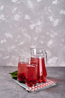 Taze vişneli limonata bardakta kağıt kamış ve gri masa zemininde sürahi, kopyalama alanı. Soğuk yaz içkisi. Meyve kokteyli.