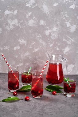 Taze vişneli limonata bardakta kağıt kamış ve gri masa zemininde sürahi, kopyalama alanı. Soğuk yaz içkisi. Meyve kokteyli.