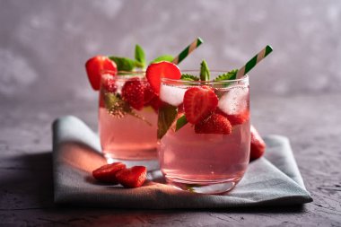 Buzlu taze çilekli limonata, nane ve kağıt kamışla gri masa arka planında köpüklü bardaklar, kopyalama alanı. Soğuk yaz içkisi. Meyve kokteyli.