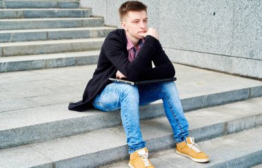 Laptop bilgisayarı olan depresyondaki bir öğrenci üniversitenin açık hava merdivenlerinde oturuyor, kopyalama alanı. Sınavlarda başarısız oldum, üniversiteden atıldım. 