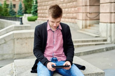 Üniversite kampüsünde oturan ve açık havada tablet bilgisayar üzerinde çalışan kendine güvenen genç bir öğrenci. Kopya alanı. Sınava hazırlanmak, daktilo etmek, internette sörf yapmak. Teknoloji, eğitim kavramı
