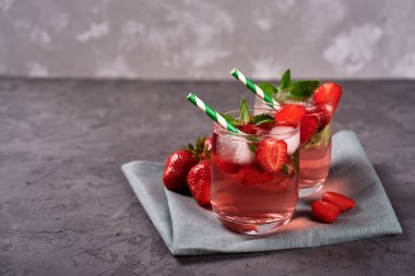 Buzlu taze çilekli limonata, nane ve kağıt kamışla gri masa arka planında köpüklü bardaklar, kopyalama alanı. Soğuk yaz içkisi. Meyve kokteyli.