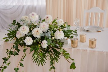 Masanın üzerinde beyaz kasımpatı çiçeklerinden oluşan bereketli bir çiçek aranjmanı. Lüks düğün süslemeleri. Restoranda düğün başkanlığı, fotokopi odası. Yeni evliler için ziyafet masası. 