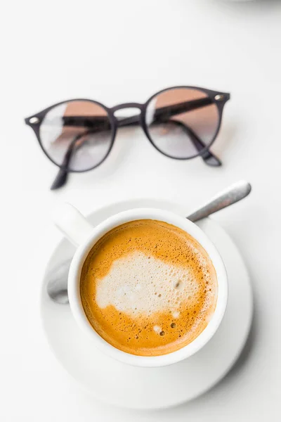 Primeros planos gafas hipster y taza de capuchino sobre mesa blanca —  Fotos de Stock