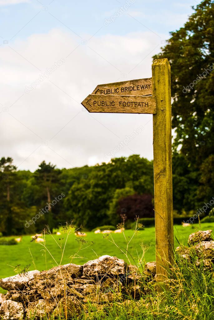 wooden public footpath sign in field next to a wall UK