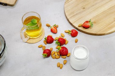 Taze süt taze çilek, badem ve sıcak bitki çayının yanında. Köyde sabah oldu. Sağlıklı bir içecek için gerekli malzemeler. Üst görünüm.