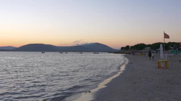 Puesta de sol en la playa de Alghero. Gente caminando por la playa . — Vídeo de stock