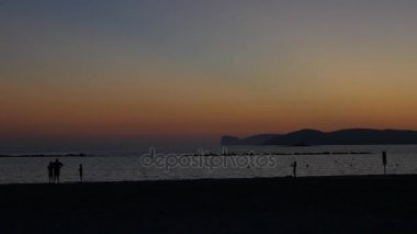 Alghero sahilde günbatımı. Sahilde yürüyüş insanlar. 
