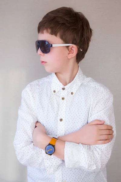 Porträtt av en ung snygg pojke i en vit skjorta, blå solglasögon och orange klocka Stockfoto