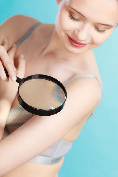 Woman using magnifying glass to examine her moles skin